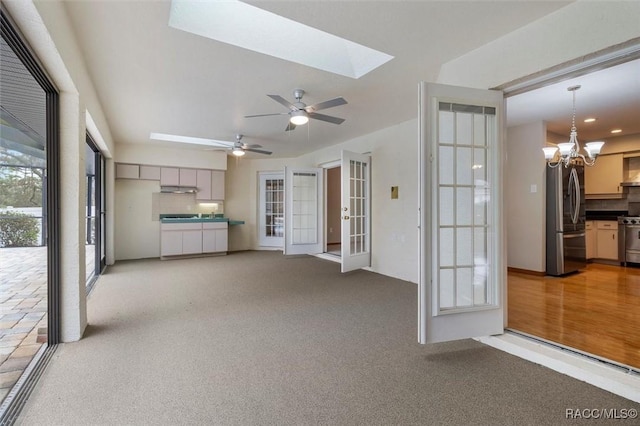 unfurnished living room featuring a skylight, light carpet, french doors, and ceiling fan with notable chandelier