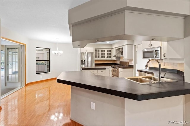 kitchen featuring kitchen peninsula, white cabinets, wall chimney range hood, and appliances with stainless steel finishes