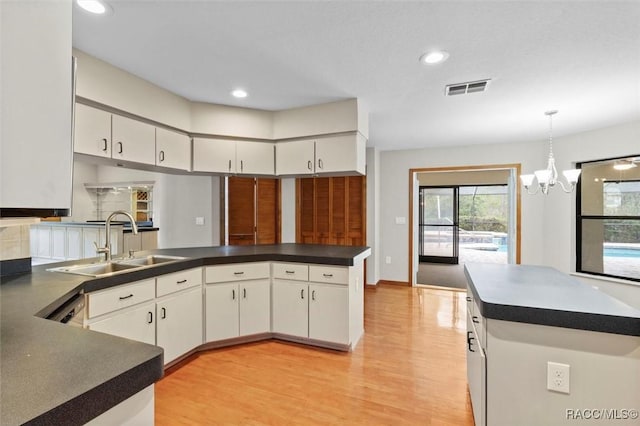 kitchen with white cabinetry, sink, kitchen peninsula, a chandelier, and decorative light fixtures