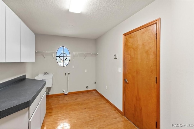 washroom with cabinets, sink, hookup for a washing machine, light hardwood / wood-style flooring, and a textured ceiling