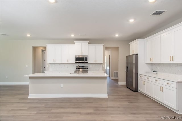 kitchen with appliances with stainless steel finishes, backsplash, light hardwood / wood-style flooring, and white cabinetry