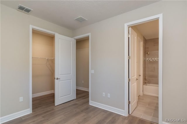 unfurnished bedroom with ensuite bathroom, a closet, a spacious closet, and light wood-type flooring