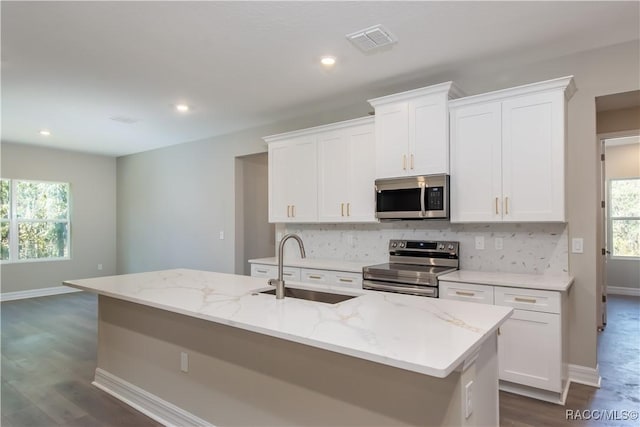 kitchen featuring stainless steel appliances, white cabinetry, a wealth of natural light, and a center island with sink