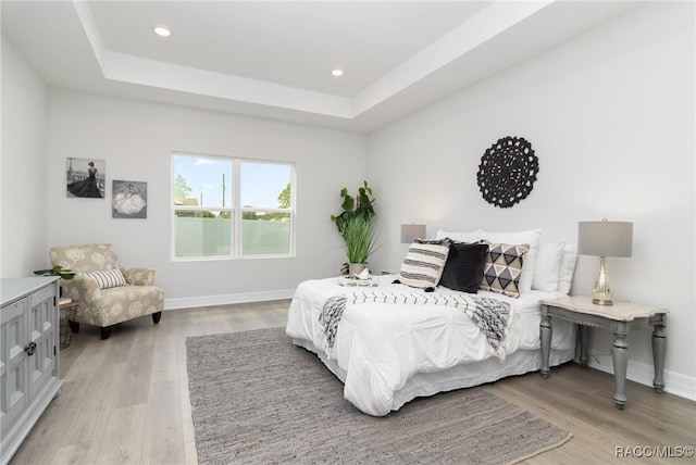 bedroom with a tray ceiling and light hardwood / wood-style flooring