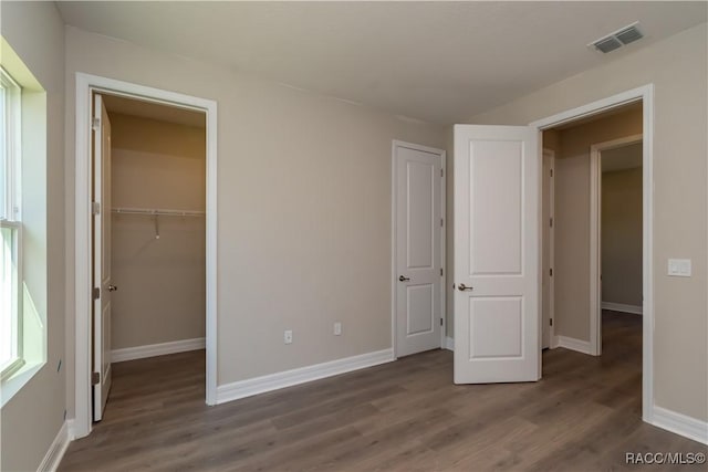 unfurnished bedroom featuring dark hardwood / wood-style flooring, a walk in closet, and a closet