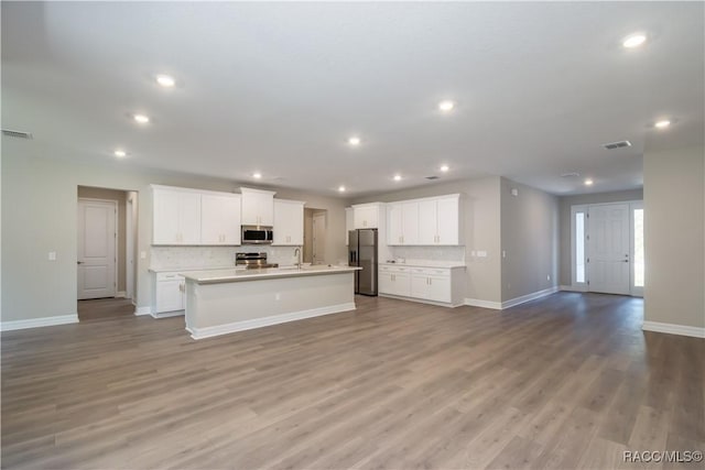 kitchen with backsplash, a kitchen island with sink, appliances with stainless steel finishes, light hardwood / wood-style floors, and white cabinetry