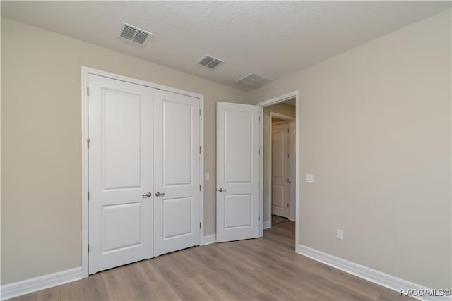 unfurnished bedroom featuring light hardwood / wood-style floors, a textured ceiling, and a closet