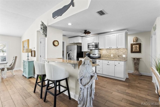 kitchen featuring lofted ceiling, white cabinets, light stone countertops, appliances with stainless steel finishes, and a kitchen bar