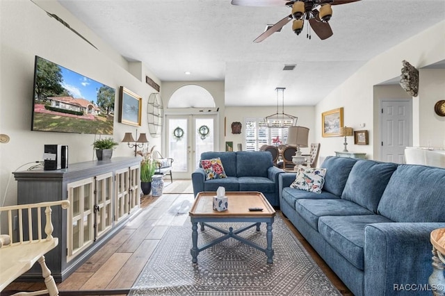 living room with a textured ceiling, lofted ceiling, french doors, and ceiling fan with notable chandelier