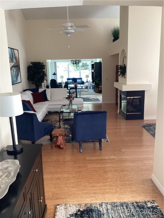 living area featuring light wood-style flooring, ceiling fan, a glass covered fireplace, and baseboards