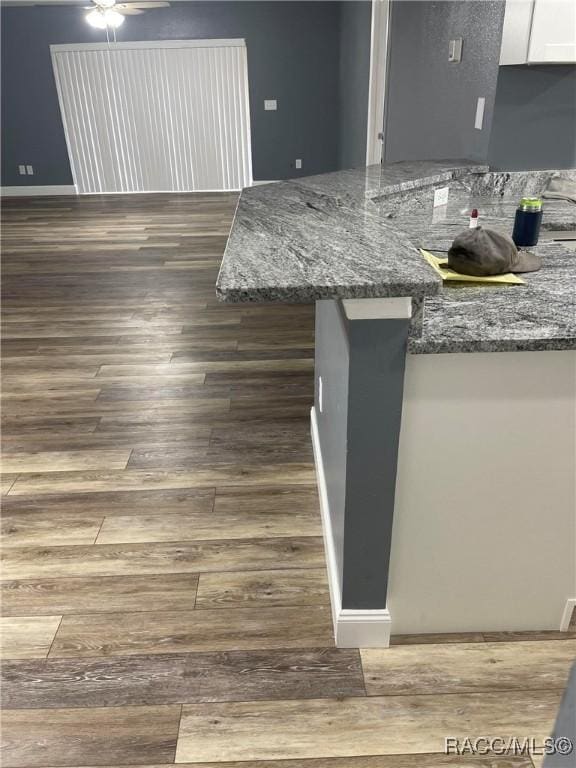 kitchen featuring dark hardwood / wood-style flooring, ceiling fan, white cabinets, and stone counters