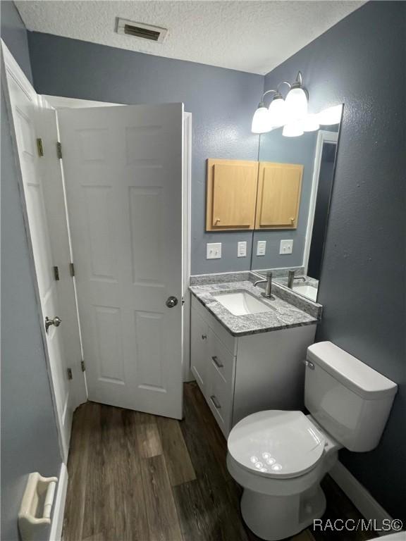 bathroom featuring wood-type flooring, toilet, a textured ceiling, and vanity