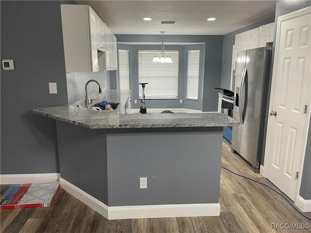 kitchen with pendant lighting, stainless steel fridge, kitchen peninsula, and white cabinets