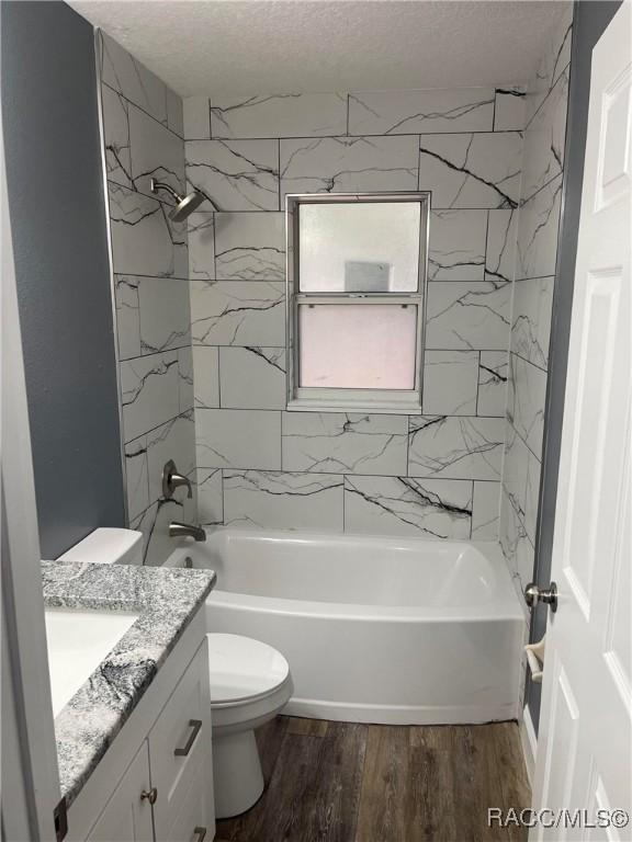 full bathroom with wood-type flooring, tiled shower / bath combo, vanity, toilet, and a textured ceiling