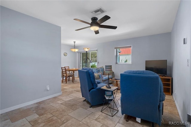 living room featuring baseboards, stone tile flooring, visible vents, and a ceiling fan