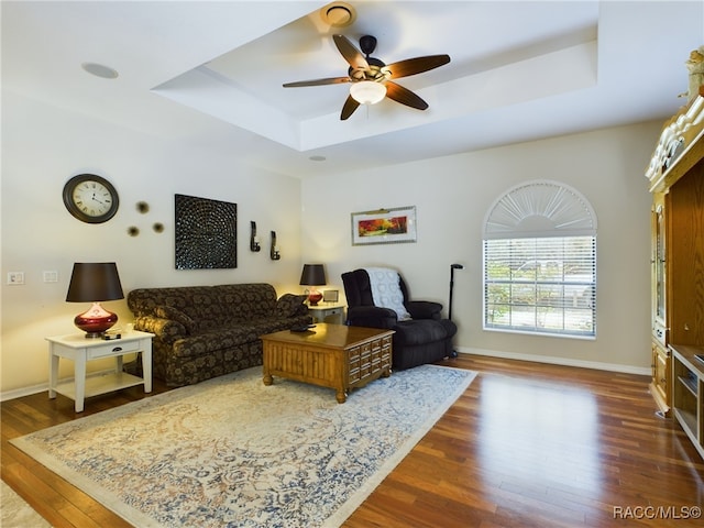 living room with a tray ceiling, ceiling fan, and dark hardwood / wood-style flooring