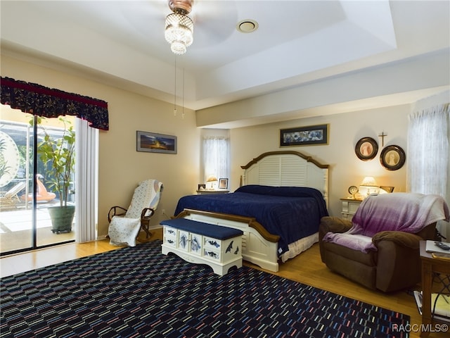 bedroom with a raised ceiling, wood-type flooring, access to outside, and multiple windows