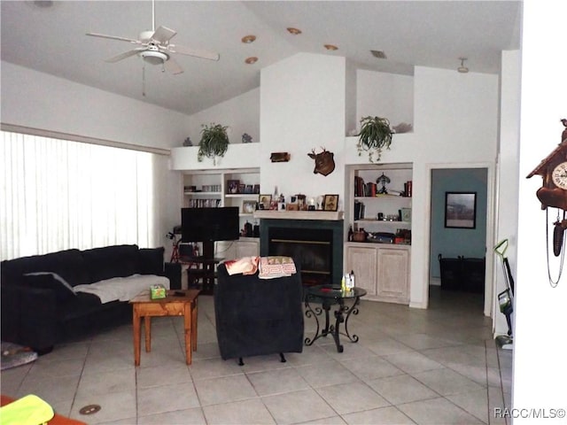 living room featuring built in shelves, light tile patterned floors, a glass covered fireplace, high vaulted ceiling, and a ceiling fan