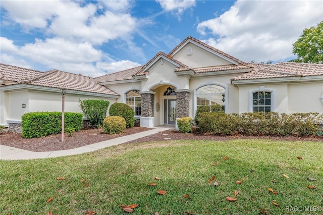 mediterranean / spanish-style home with a tile roof, stucco siding, and a front lawn