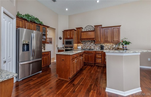kitchen with dark wood-type flooring, decorative backsplash, glass insert cabinets, a kitchen island, and appliances with stainless steel finishes