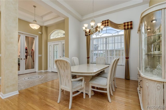 dining room with light wood-style floors, french doors, a raised ceiling, and a notable chandelier