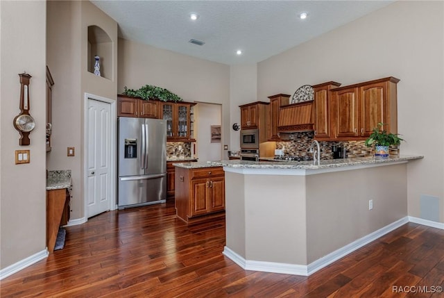 kitchen with brown cabinetry, stainless steel appliances, decorative backsplash, and dark wood finished floors
