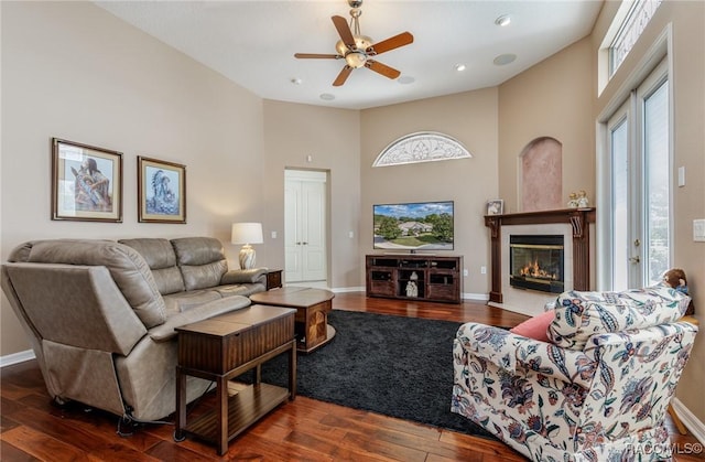 living room with wood finished floors, a ceiling fan, a high ceiling, baseboards, and a glass covered fireplace