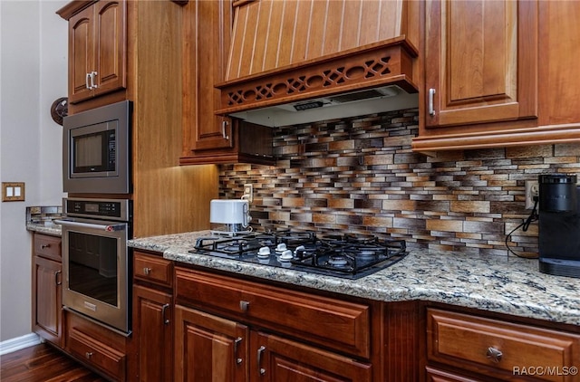 kitchen with light stone counters, premium range hood, appliances with stainless steel finishes, and tasteful backsplash