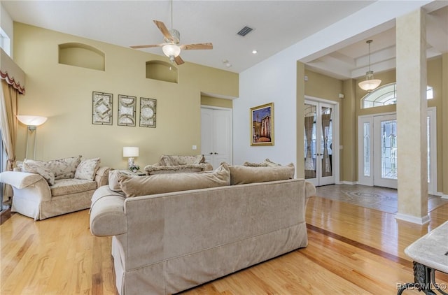 living room with a towering ceiling, a ceiling fan, visible vents, and wood finished floors