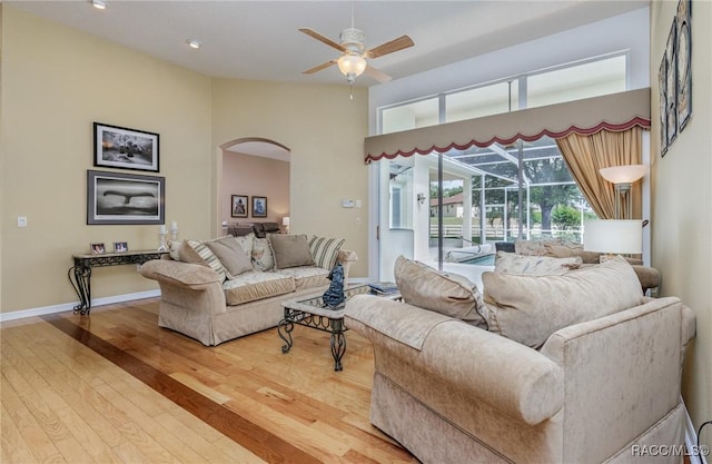 living area featuring wood finished floors, arched walkways, a ceiling fan, a sunroom, and a high ceiling