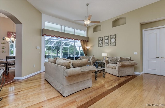 living room with arched walkways, baseboards, wood-type flooring, and ceiling fan with notable chandelier