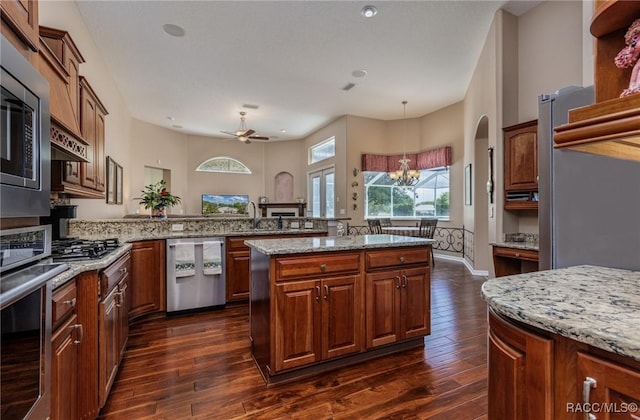 kitchen featuring dark wood-style flooring, light stone counters, ceiling fan with notable chandelier, a peninsula, and appliances with stainless steel finishes