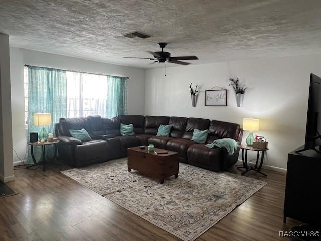 living room featuring ceiling fan, dark hardwood / wood-style floors, and a textured ceiling