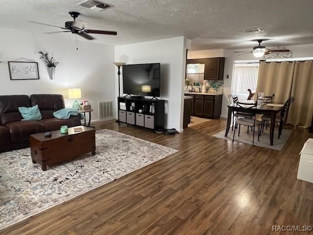 living room featuring ceiling fan, dark wood-type flooring, and a textured ceiling