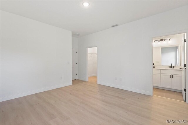 unfurnished bedroom with light wood-style flooring, a sink, visible vents, baseboards, and a walk in closet