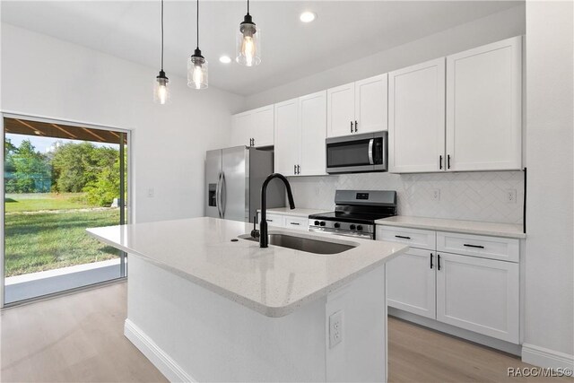 kitchen with a sink, stainless steel appliances, a center island with sink, light wood-type flooring, and backsplash
