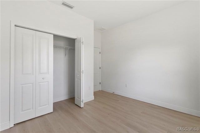 unfurnished bedroom featuring baseboards, visible vents, light wood-type flooring, and a closet