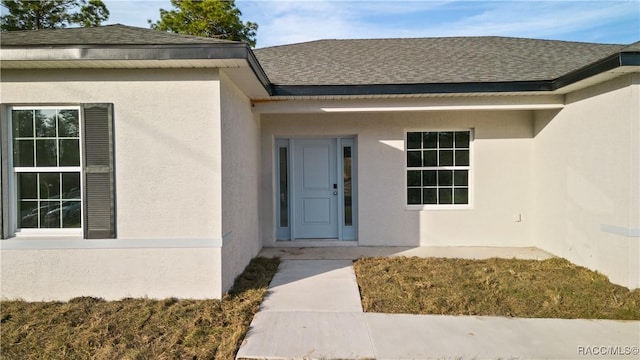 doorway to property with a shingled roof and stucco siding