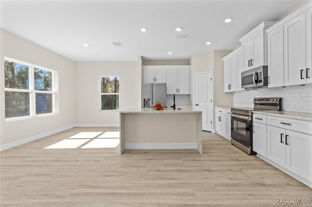 kitchen with light wood-type flooring, white cabinetry, stainless steel appliances, a kitchen island with sink, and decorative backsplash