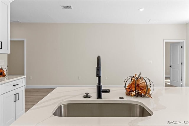 kitchen featuring wood-type flooring, white cabinetry, sink, and light stone countertops