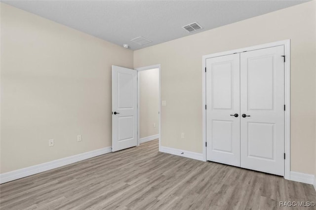 unfurnished bedroom featuring light hardwood / wood-style flooring, a textured ceiling, and a closet