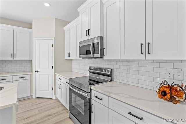 kitchen with light hardwood / wood-style flooring, stainless steel appliances, light stone counters, backsplash, and white cabinetry