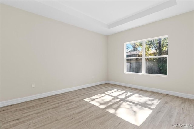 spare room featuring a tray ceiling and light hardwood / wood-style floors