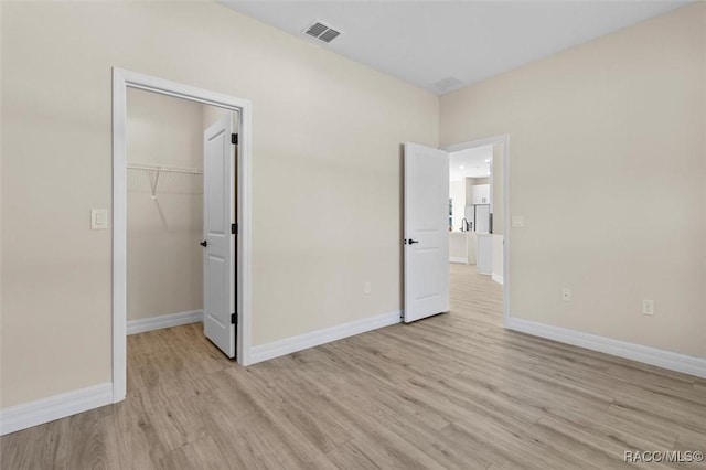 unfurnished bedroom with a closet, a walk in closet, and light hardwood / wood-style floors