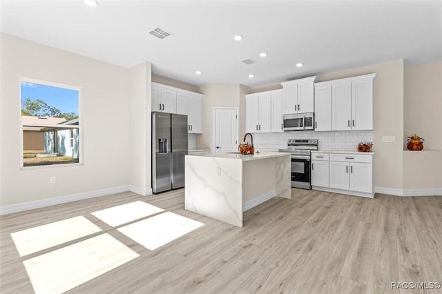 kitchen with white cabinets, an island with sink, stainless steel appliances, and light stone counters