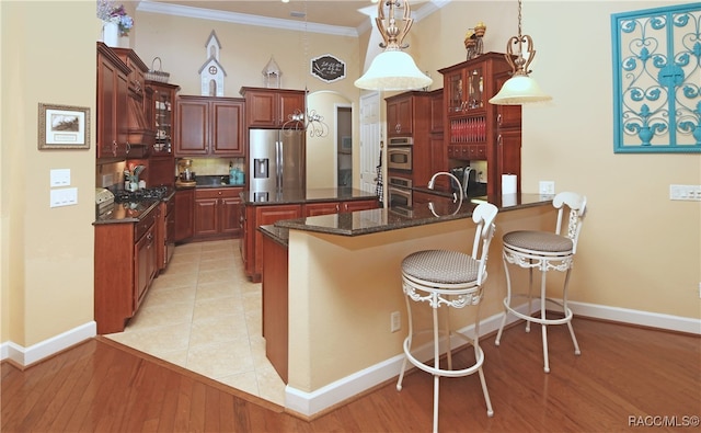 kitchen featuring stainless steel appliances, a kitchen breakfast bar, light hardwood / wood-style floors, decorative light fixtures, and ornamental molding