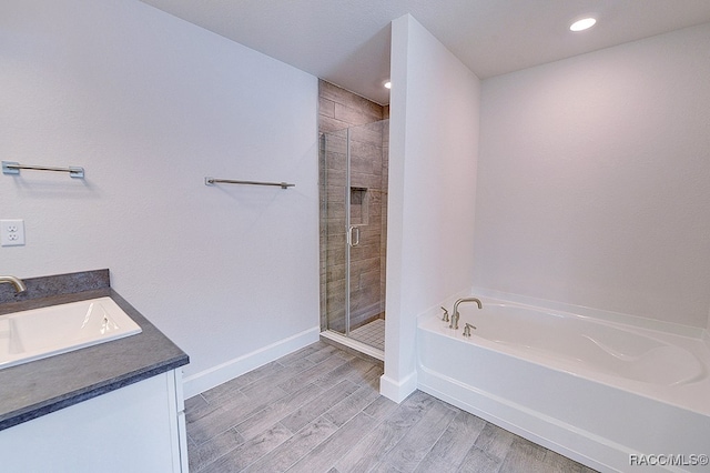 bathroom featuring plus walk in shower, vanity, and wood-type flooring