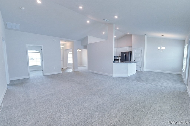 unfurnished living room featuring light colored carpet, vaulted ceiling, and a notable chandelier