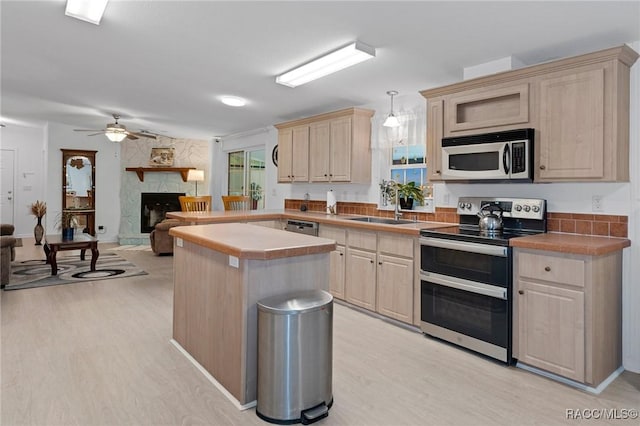 kitchen with stainless steel appliances, sink, decorative light fixtures, light brown cabinets, and a stone fireplace