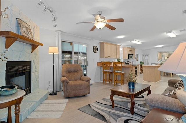 living room with ceiling fan, light hardwood / wood-style flooring, and a stone fireplace